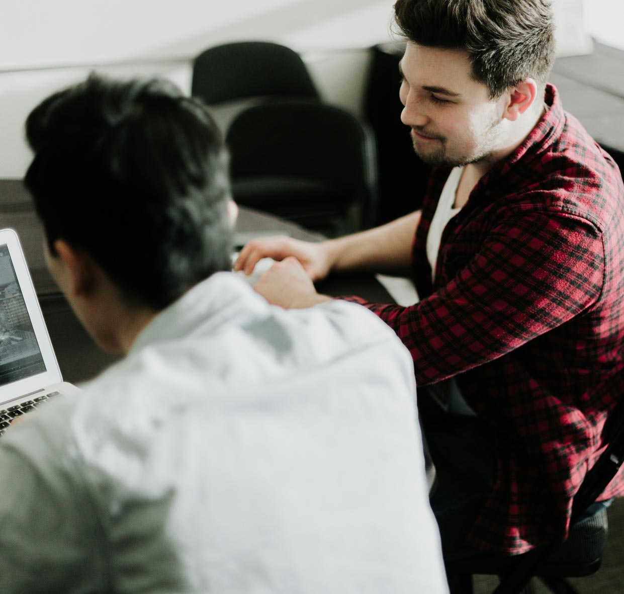 Two people are collaborating in an office setting, looking at a laptop screen together.