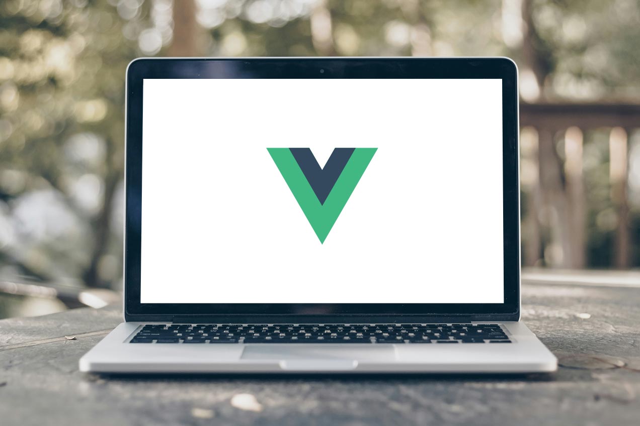 A laptop on a wooden table outdoors displays the Vue JS logo on its screen, with blurred greenery in the background.